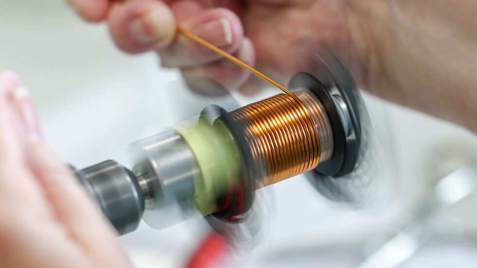 An einer Maschine wickelt eine Mitarbeiterin eine Spule für eine PFC-Drossel. An einer Maschine wickelt eine Mitarbeiterin eine Spule für eine PFC-Drossel.