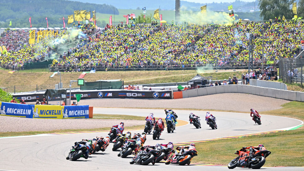 Das Fahrerfeld passiert die erste Kurve vor dem Fanblock. 